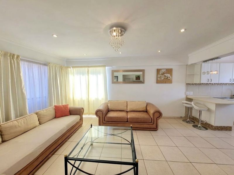 Spacious open-plan living area featuring tiled flooring, recessed lighting, and a functional kitchen with a breakfast bar and white cabinetry.
