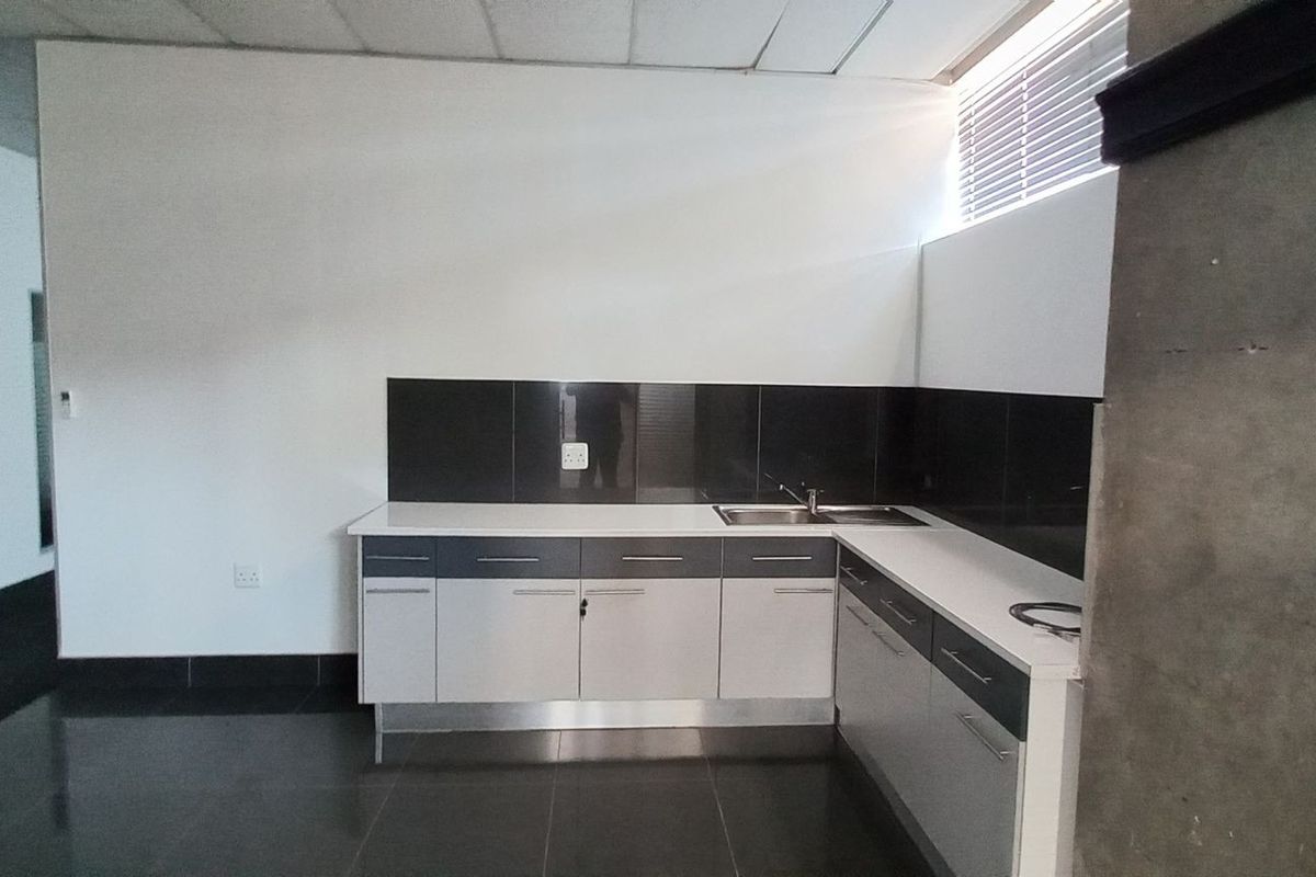 A functional kitchenette area featuring modern cabinetry, a stainless steel sink, and dark tiled splashbacks within an industrial office space.