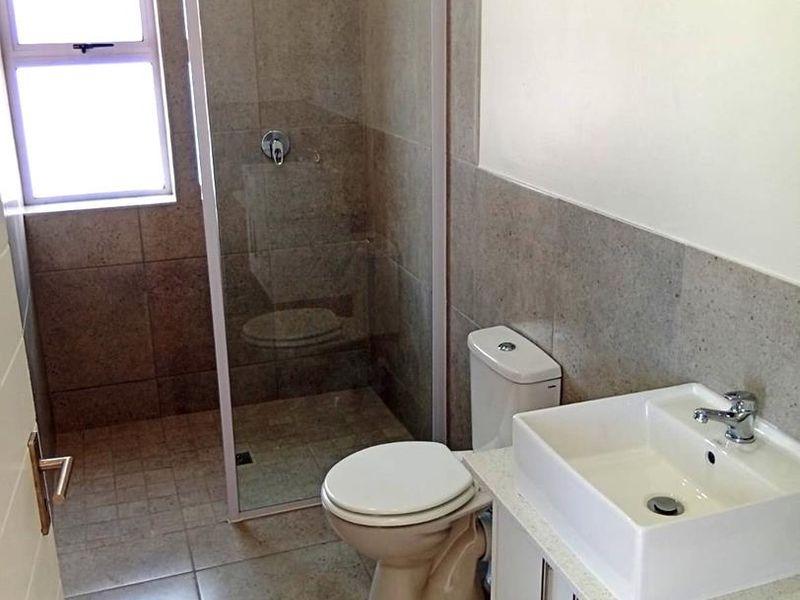 A clean, modern bathroom featuring a glass-enclosed shower, a white vanity with a vessel sink, and neutral floor-to-ceiling wall tiles.