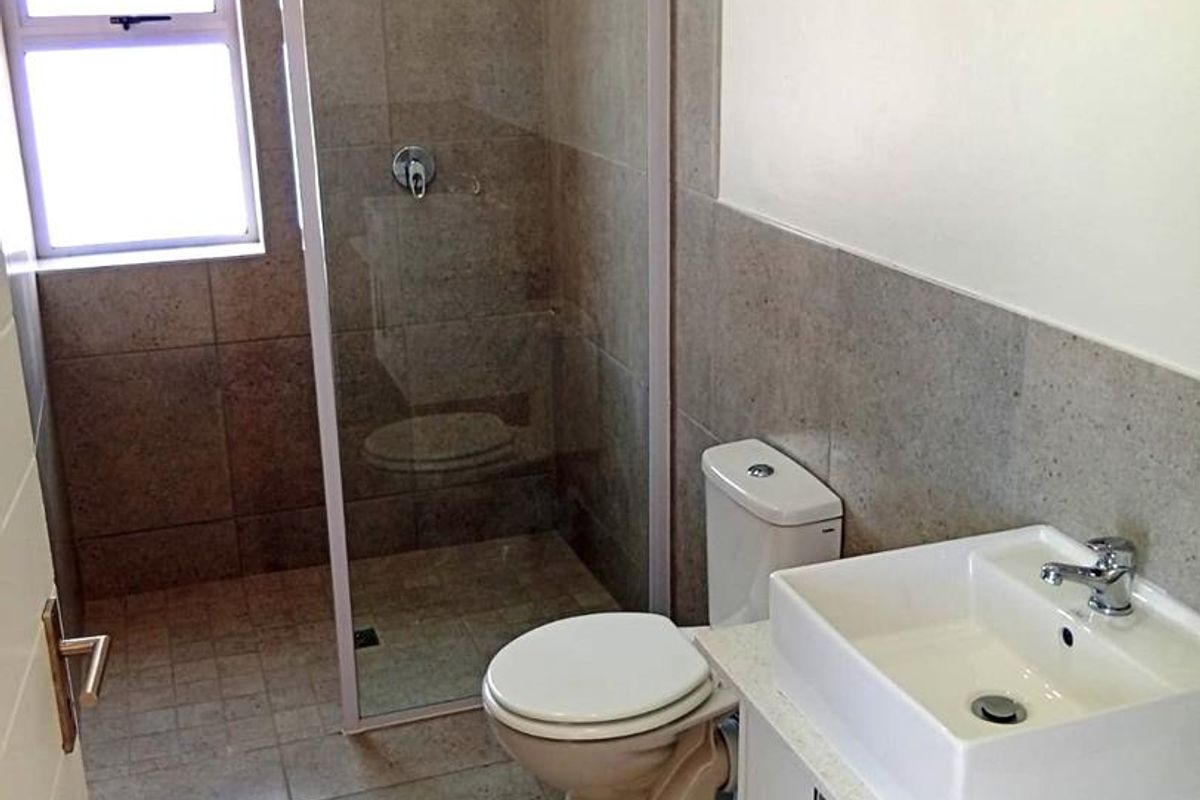A clean, modern bathroom featuring a glass-enclosed shower, a white vanity with a vessel sink, and neutral floor-to-ceiling wall tiles.