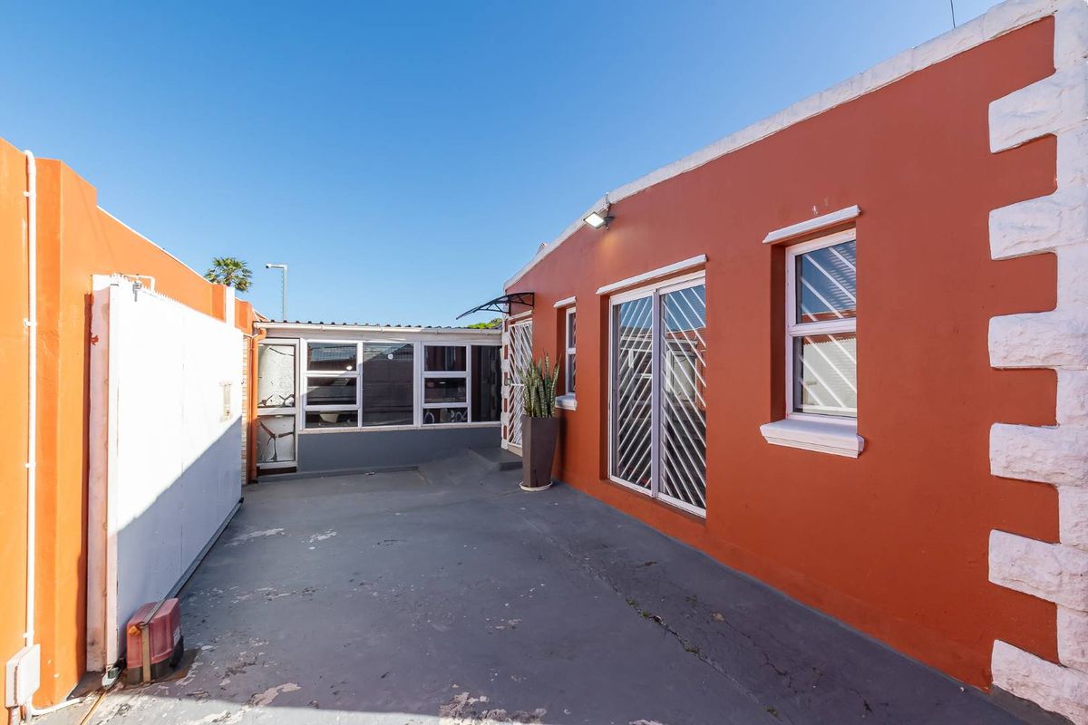A rear exterior view of the property featuring a concrete patio area, security gates, and painted exterior walls.