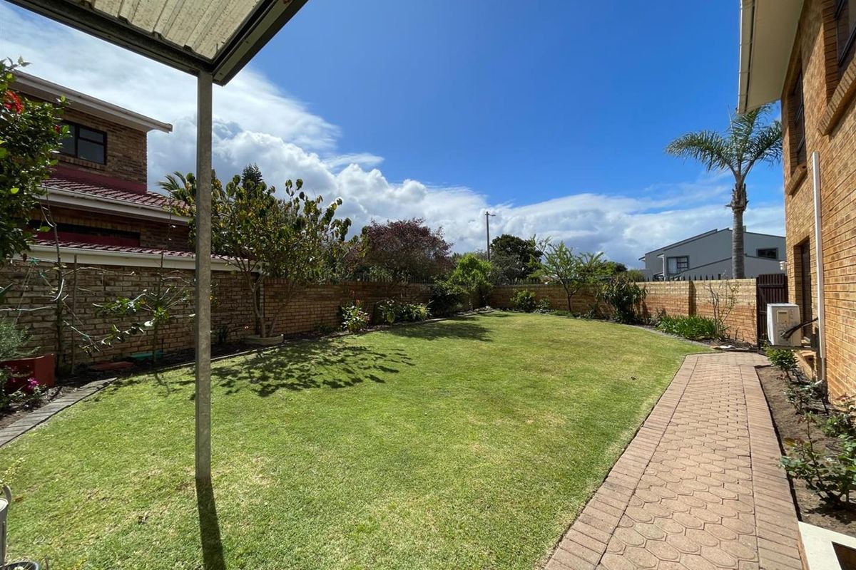A well-maintained rear garden featuring a paved walkway, established lawn, and perimeter brick boundary walls.