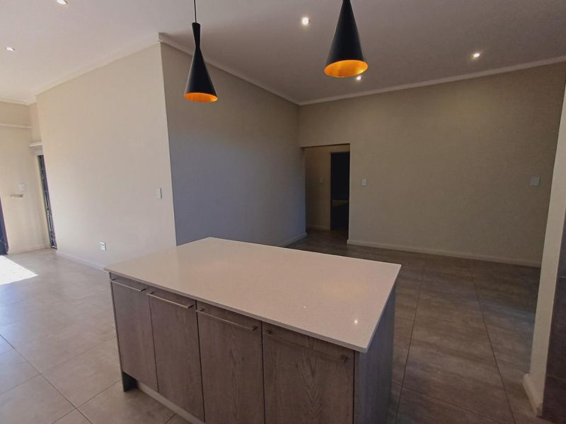 A modern, empty kitchen area featuring a central island with a stone countertop, neutral tiled flooring, and recessed ceiling lighting.