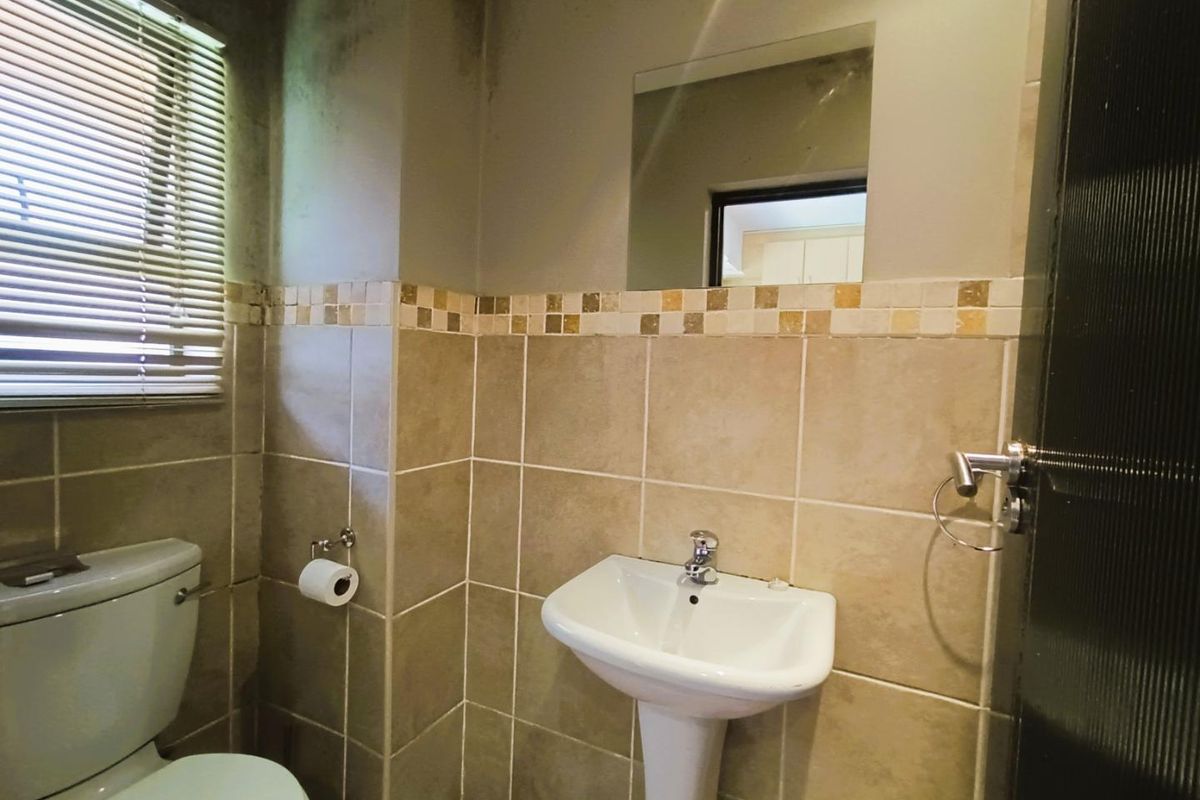 A compact bathroom featuring a pedestal basin, toilet, and tiled walls with a window and integrated mirror.