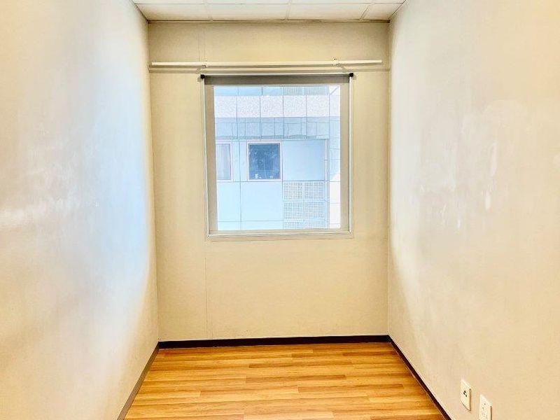 A small, empty office space featuring laminate flooring, a drop ceiling, and a window, suitable for a home workspace or study.