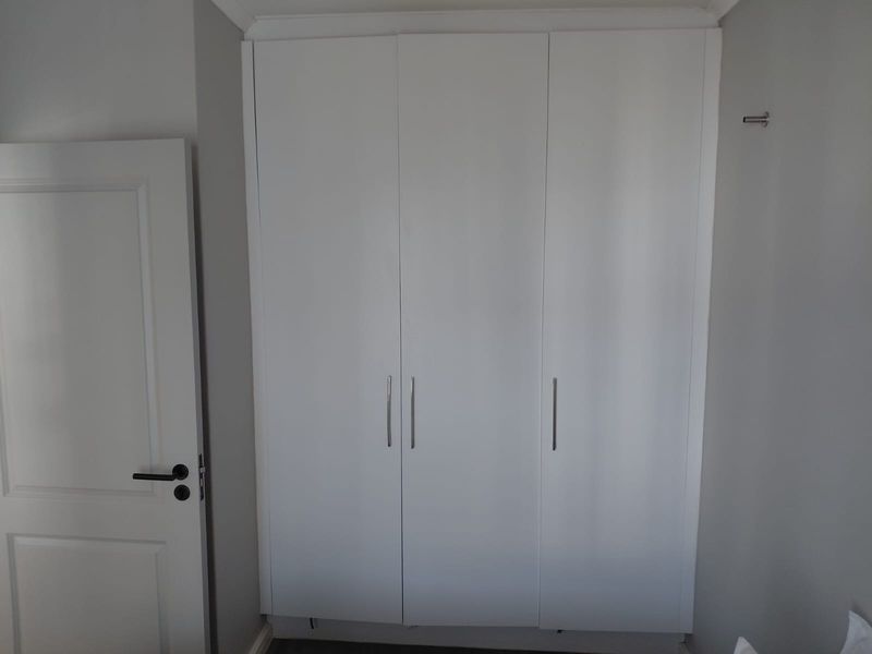 A clean bedroom interior featuring a modern white built-in wardrobe and a matching internal door with contemporary hardware.