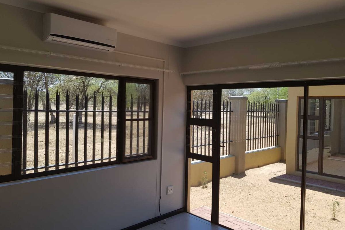 A bright, empty living area featuring tiled flooring, a wall-mounted air conditioning unit, and large sliding glass doors providing access to the exterior.