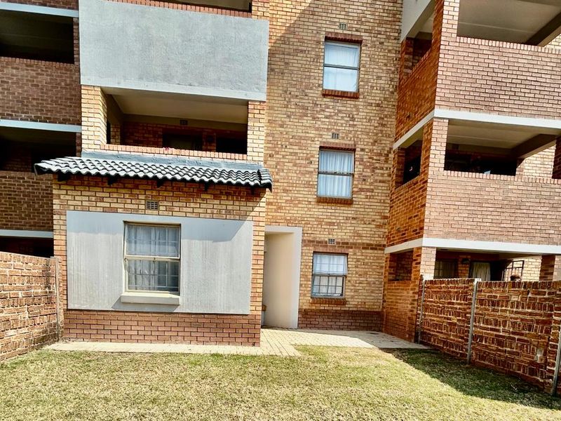 Rear view of a multi-story apartment building featuring face brick construction, private balconies, and a small paved courtyard area with boundary walls.