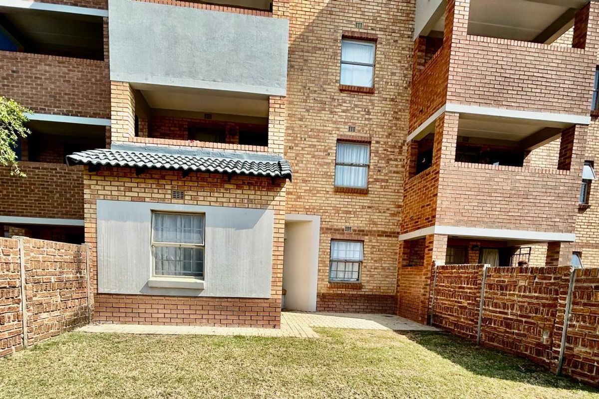 Rear view of a multi-story apartment building featuring face brick construction, private balconies, and a small paved courtyard area with boundary walls.