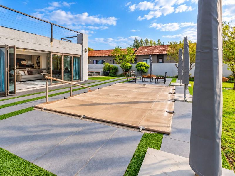 A well-maintained outdoor pool area featuring a covered swimming pool, paved patio, and seamless indoor-outdoor flow through large bi-fold doors.