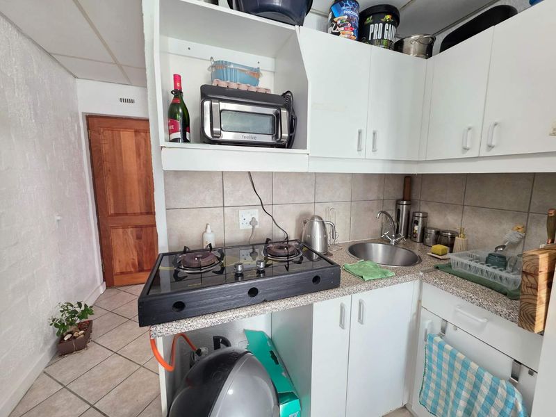 Compact kitchen featuring white cabinetry, a gas hob, stainless steel sink, and tiled backsplash, requiring cosmetic updates to improve functionality and aesthetic appeal.