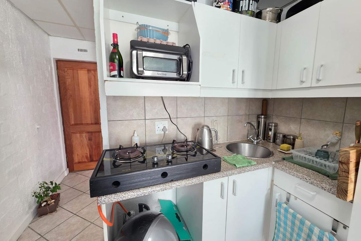 Compact kitchen featuring white cabinetry, a gas hob, stainless steel sink, and tiled backsplash, requiring cosmetic updates to improve functionality and aesthetic appeal.