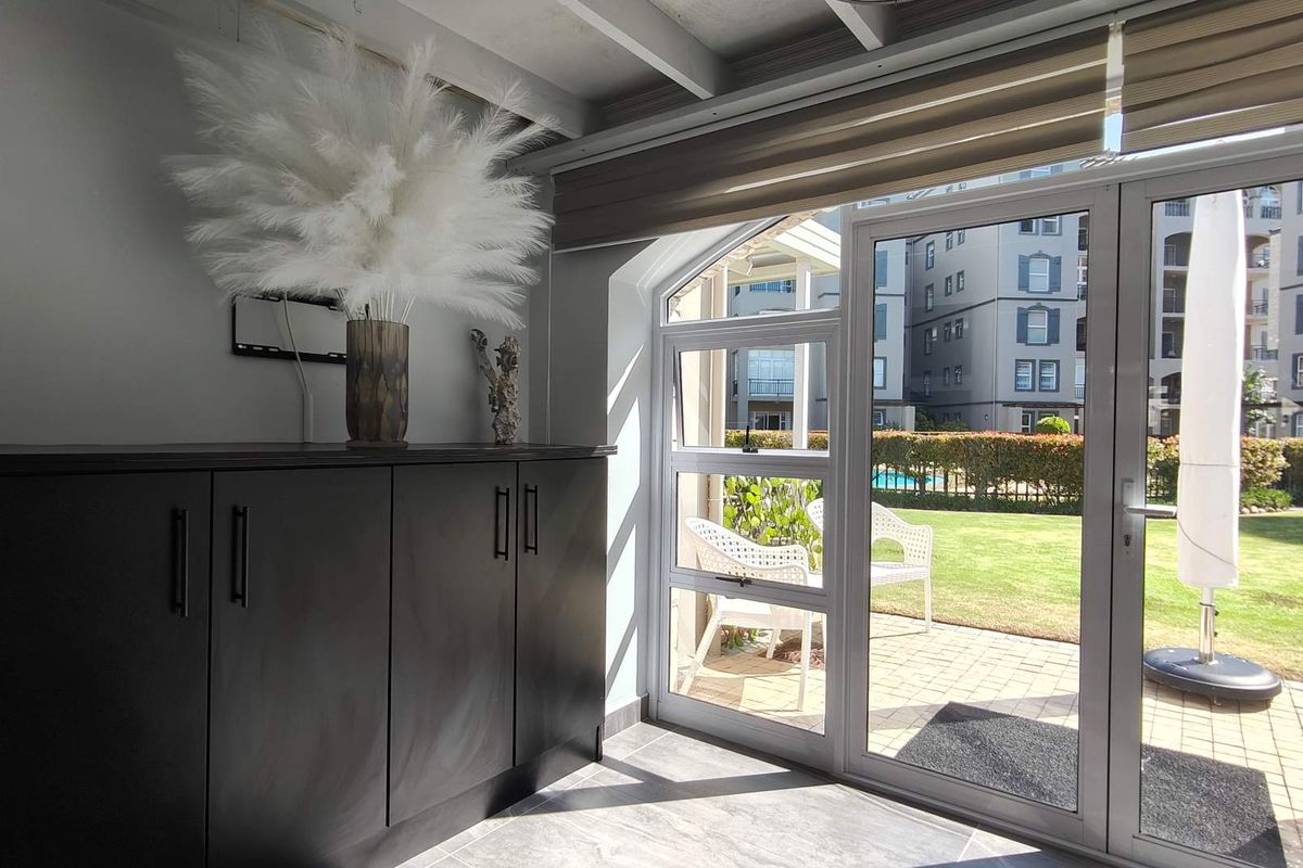 A bright living area featuring built-in cabinetry and large glass doors providing seamless access to a paved patio and garden area.