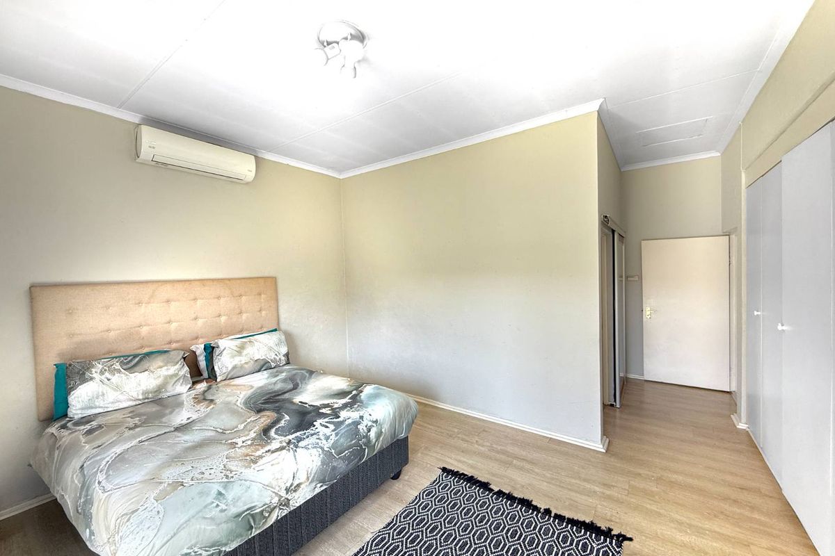 A bedroom featuring light wood-look flooring, built-in cupboards, and a wall-mounted air conditioning unit.