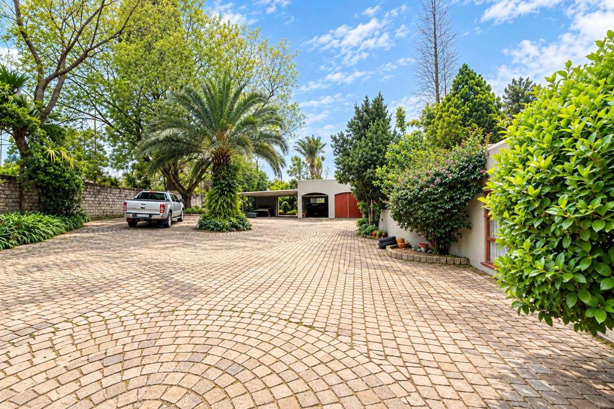 Spacious front exterior featuring a circular cobblestone driveway, mature landscaping, and a multi-car carport and garage structure.