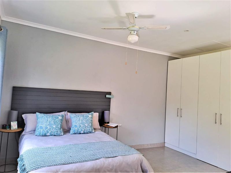 A well-maintained bedroom featuring neutral wall tones, a ceiling fan, and ample storage provided by a large built-in wardrobe.