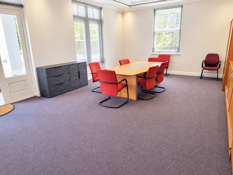 A well-lit office space featuring built-in cabinetry, carpeted flooring, and direct access to an outdoor patio area through a glass door.
