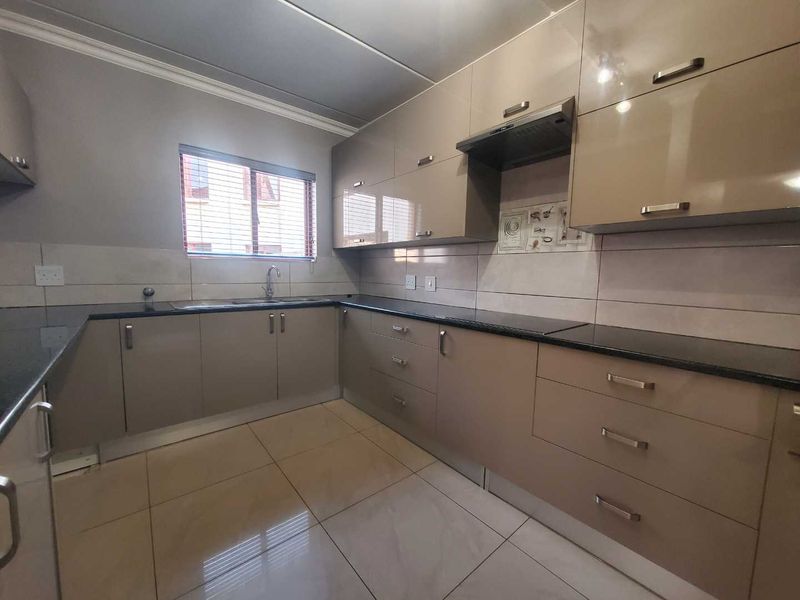 A modern, well-maintained kitchen featuring glossy cabinetry, granite countertops, a tiled backsplash, and neutral floor tiles, offering a clean and functional workspace.