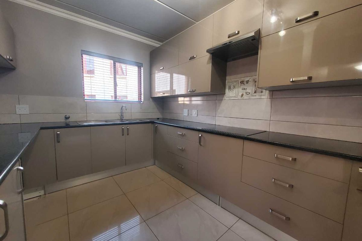A modern, well-maintained kitchen featuring glossy cabinetry, granite countertops, a tiled backsplash, and neutral floor tiles, offering a clean and functional workspace.