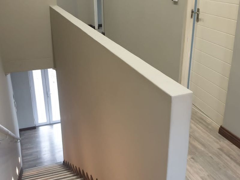 A bright, modern hallway and staircase area featuring neutral wall tones, laminate flooring, and clean architectural lines.