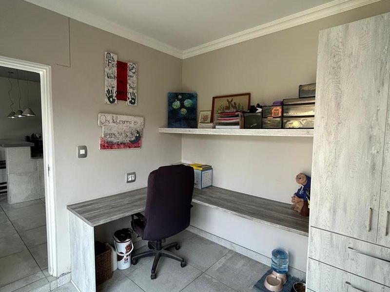 A functional home office featuring built-in desk space, integrated shelving, and cabinetry with neutral tiled flooring.
