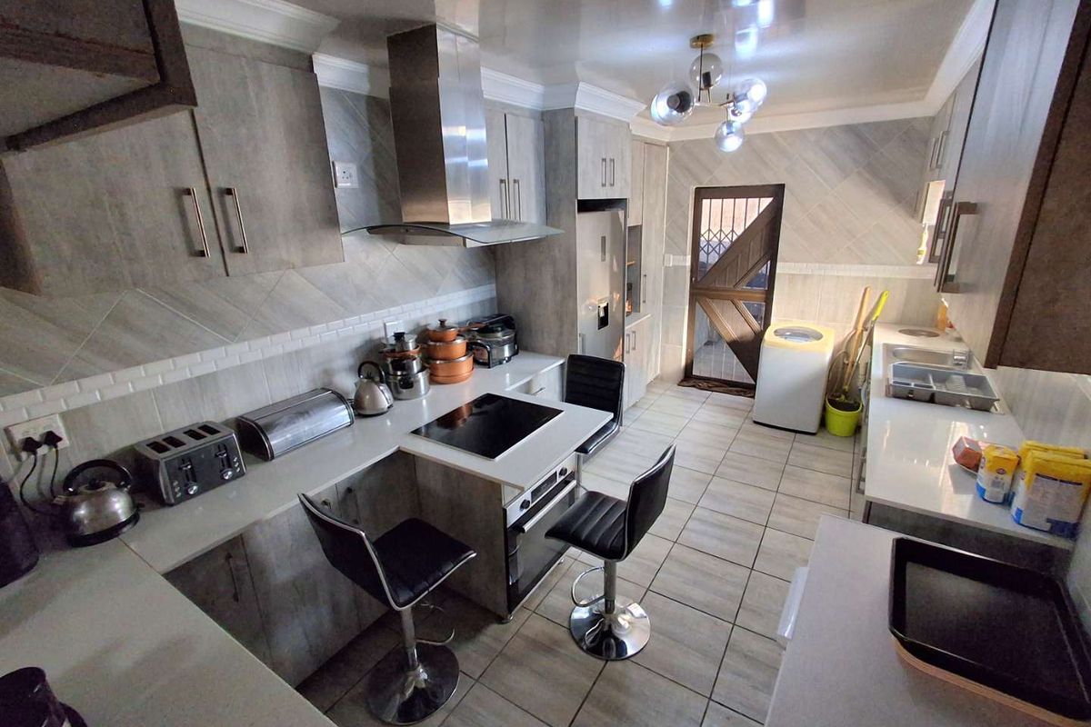 Modern kitchen featuring grey cabinetry, stone countertops, built-in hob, extractor fan, and tiled flooring with an integrated laundry area.