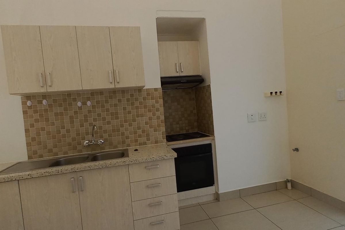 A functional kitchen featuring light wood-finish cabinetry, mosaic tile backsplash, built-in oven with hob, and tiled flooring. The space is clean and ready for use.