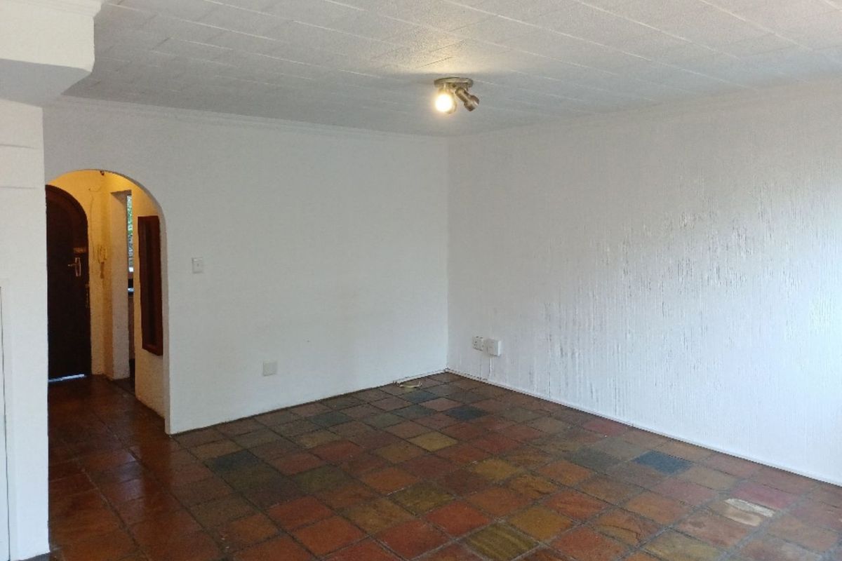 An empty living area featuring traditional terracotta-style floor tiles, an arched doorway, and a textured wall finish.