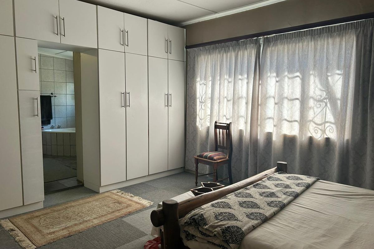 A bedroom featuring extensive built-in white cabinetry and an en-suite bathroom access, with neutral carpeting and natural light through large windows.
