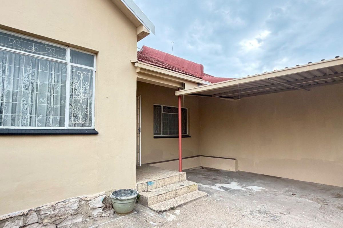 Exterior view of the property featuring a covered patio area, tiled entrance steps, and a concrete driveway.