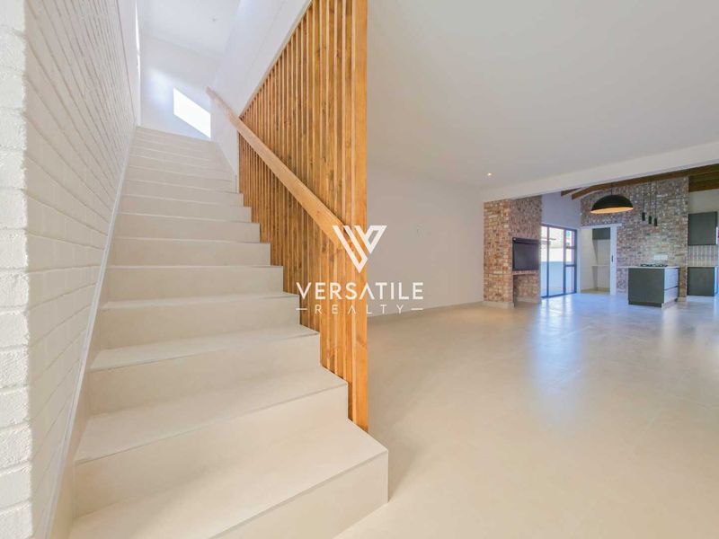 Spacious open-plan living area featuring a modern staircase with timber slat balustrade, exposed brick accents, and sleek tiled flooring throughout.