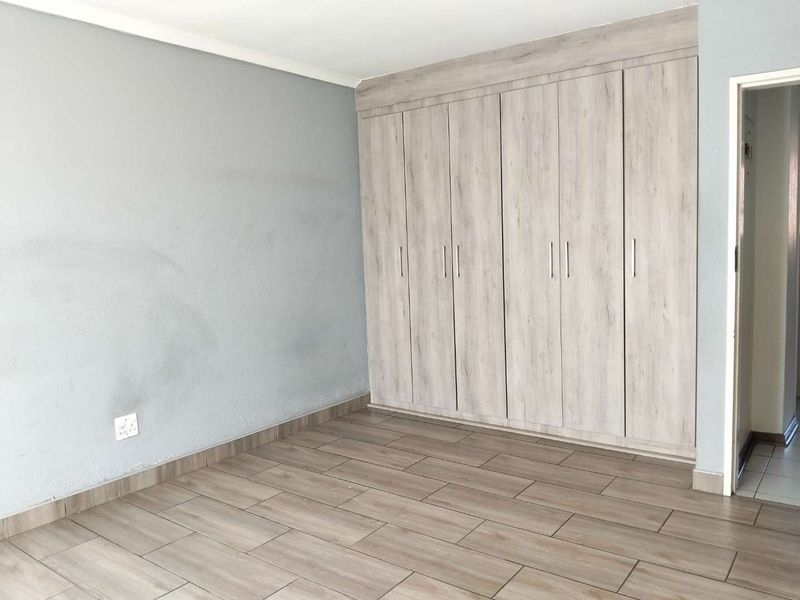 A vacant bedroom featuring light wood-look tiled flooring and extensive built-in cupboards with a modern finish.