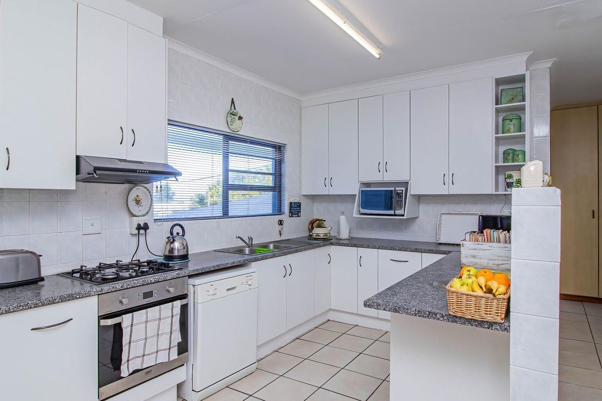A functional kitchen featuring white cabinetry, granite-look countertops, a built-in oven with gas hob, extractor fan, and tiled flooring.