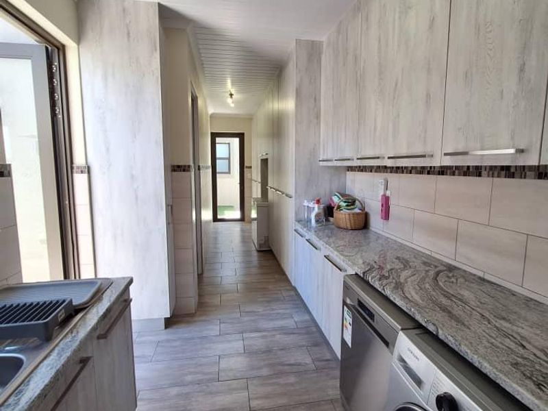 A well-appointed laundry room featuring extensive built-in cabinetry, stone countertops, tiled backsplash, and modern tiled flooring with direct access to the exterior.