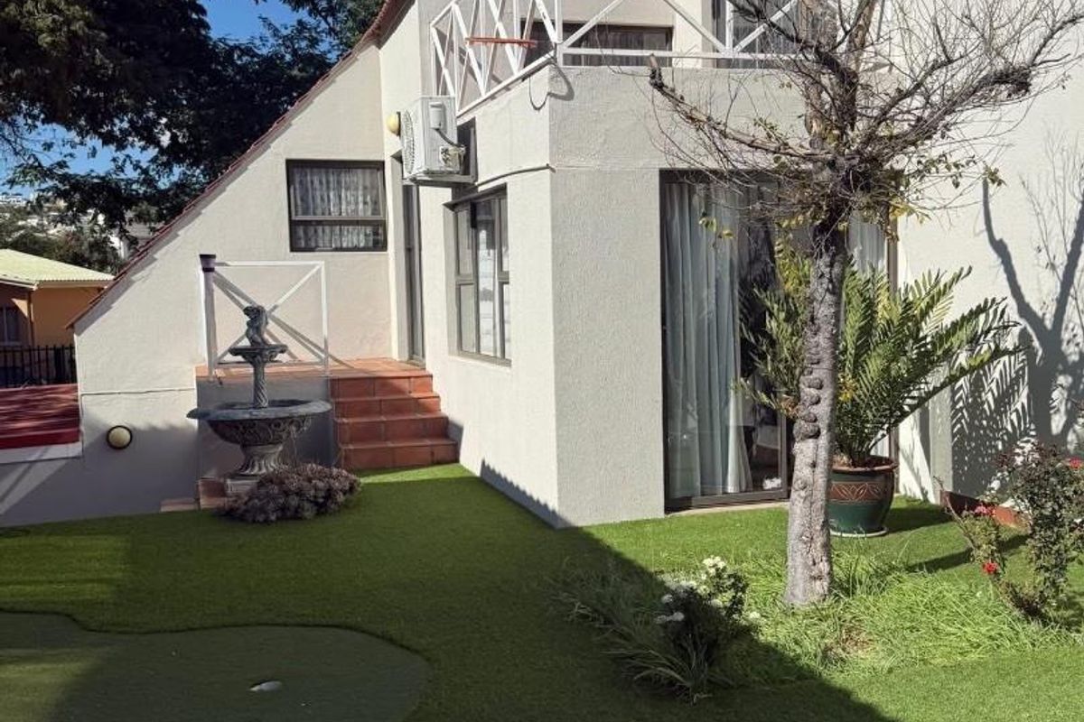 Rear view of the property featuring a landscaped garden with artificial turf, a small putting green, and an elevated balcony with metal railings.