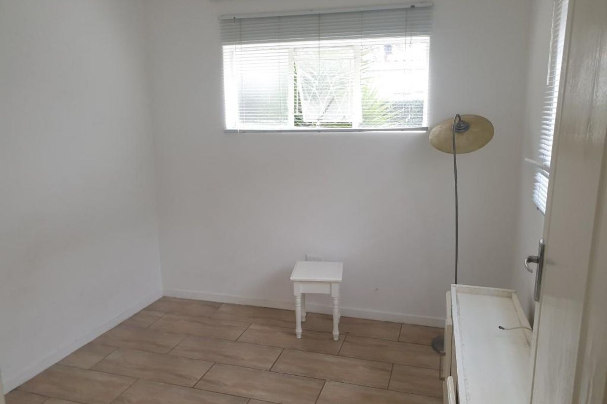 A bright, empty bedroom featuring neutral tiled flooring and fitted venetian blinds, offering a clean canvas for personalization.