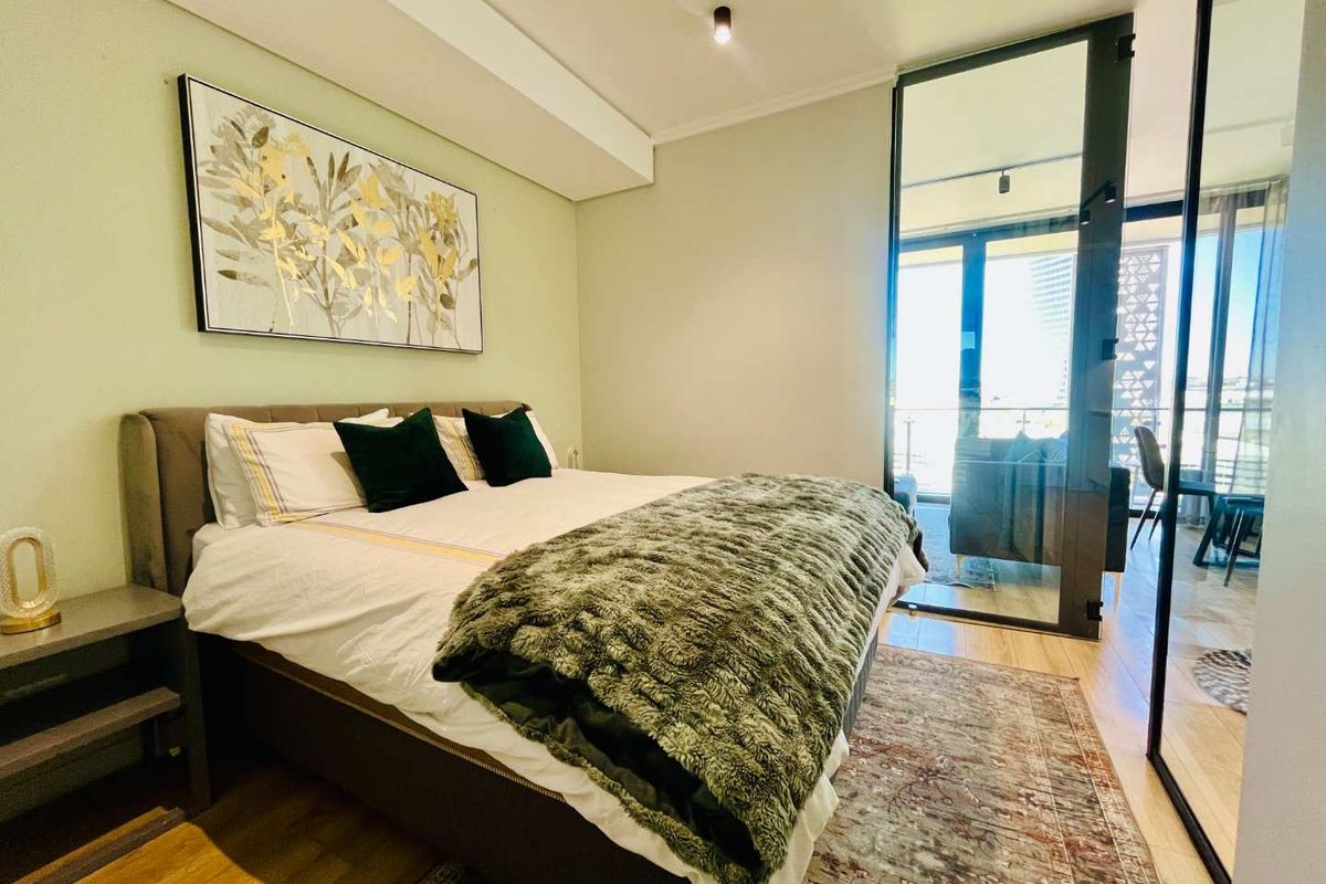 A modern bedroom featuring laminate flooring, recessed lighting, and a sleek glass partition wall providing a view into the adjacent living area.