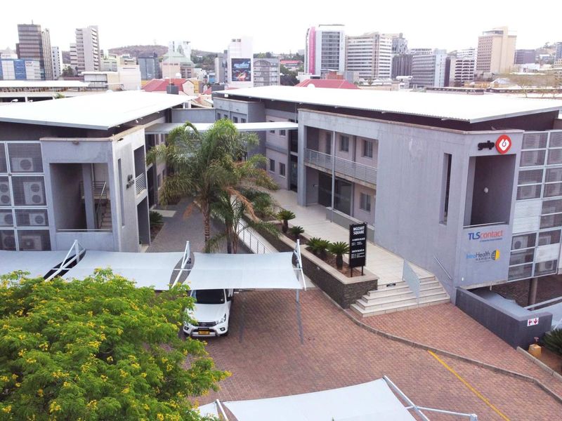 Aerial view of a modern multi-story office complex featuring paved parking areas, shade cloth carports, and landscaped courtyards in an urban setting.