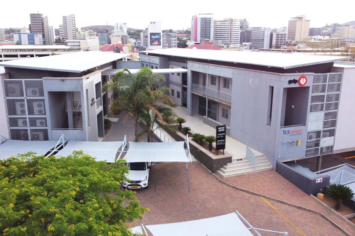 Aerial view of a modern multi-story office complex featuring paved parking areas, shade cloth carports, and landscaped courtyards in an urban setting.