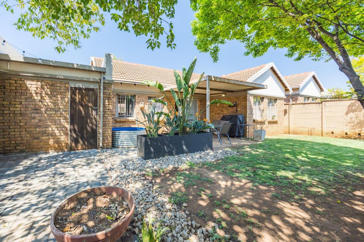 Rear view of the townhouse featuring a covered patio, brick exterior, paved walkway, and a private garden area with mature trees.