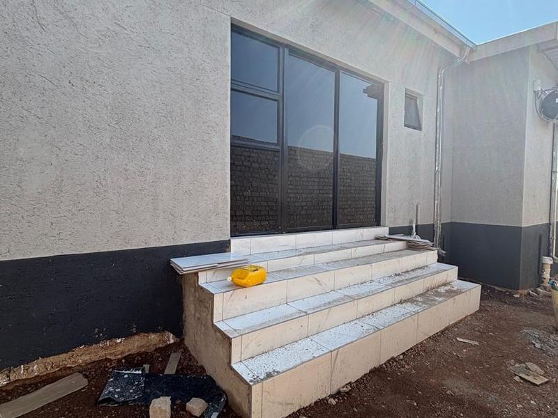 Rear exterior view showing a sliding glass door with newly installed tiled steps and unfinished surrounding ground area.