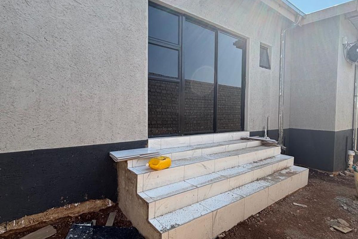 Rear exterior view showing a sliding glass door with newly installed tiled steps and unfinished surrounding ground area.
