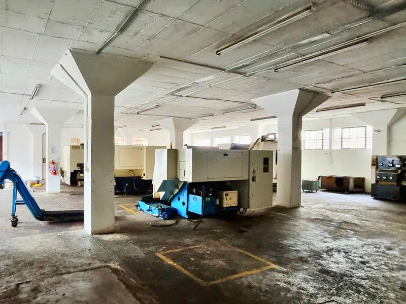 Spacious industrial utility area featuring concrete flooring, structural columns, and overhead fluorescent lighting, suitable for manufacturing or storage operations.