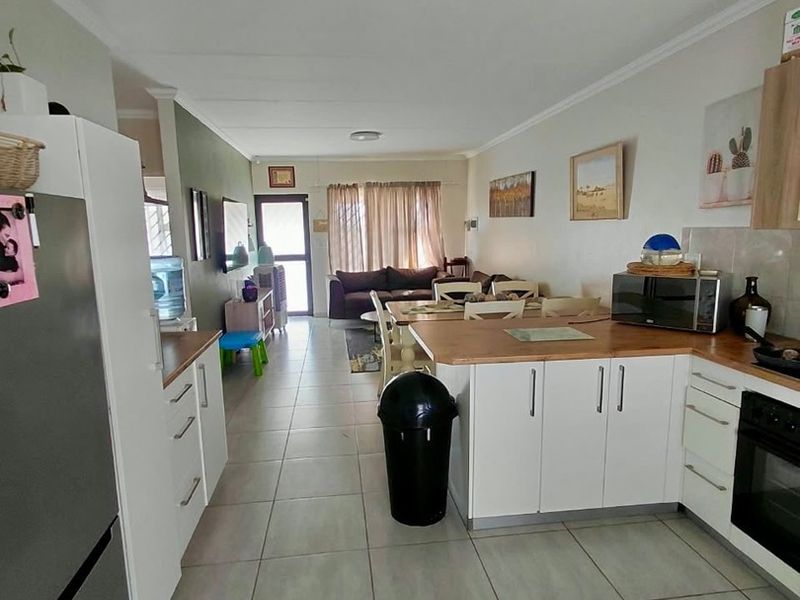 Open-plan living and kitchen area featuring tiled flooring, white cabinetry with wooden countertops, and a built-in oven, creating a functional combined space.
