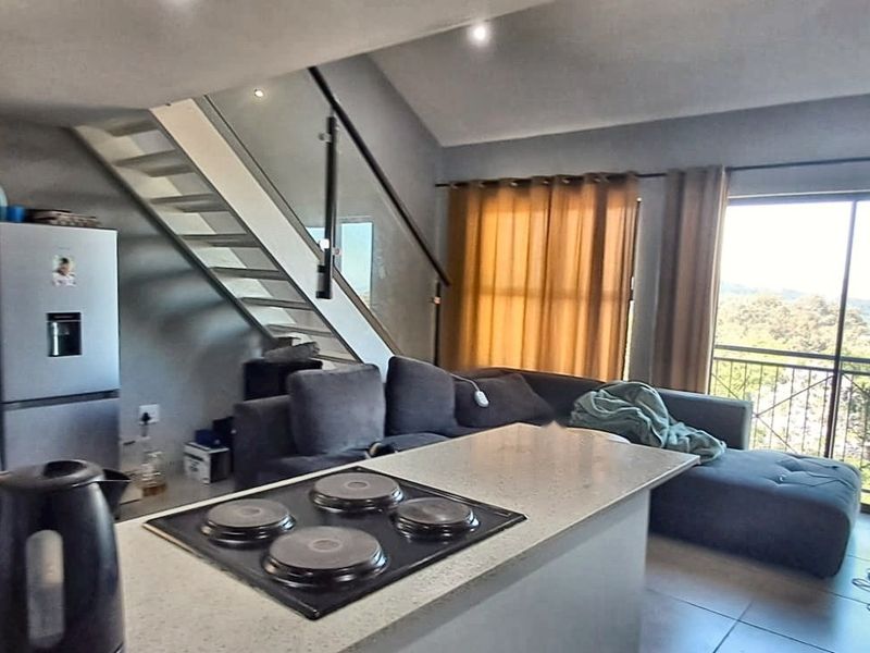 Open-plan living area featuring a kitchen island with an integrated hob, a modern staircase with glass balustrade, and access to a balcony.