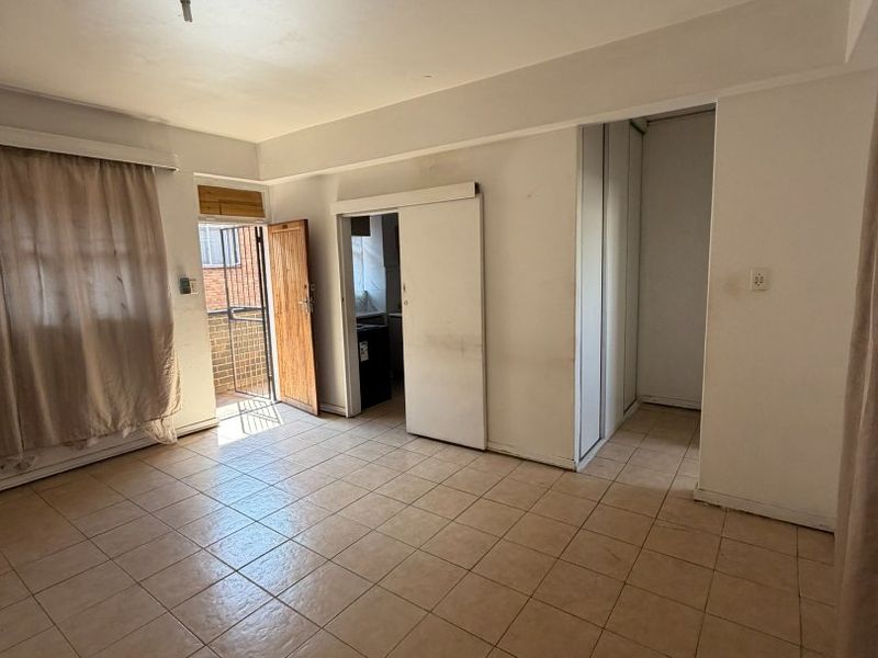 An empty living area featuring tiled flooring, built-in storage, and direct access to an exterior balcony through a sliding door.