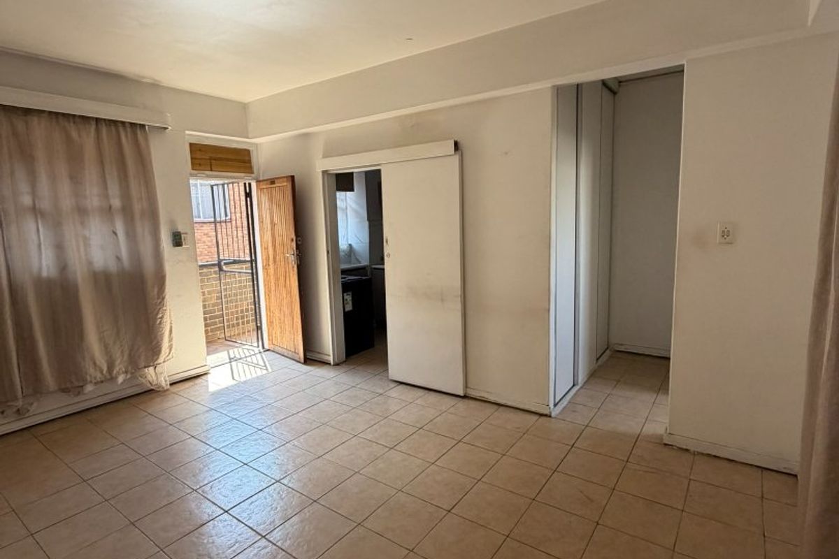 An empty living area featuring tiled flooring, built-in storage, and direct access to an exterior balcony through a sliding door.