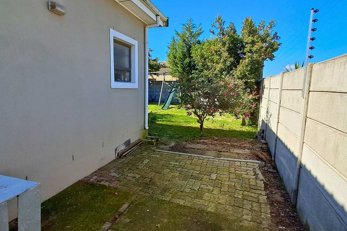 A side garden area featuring paved sections, a boundary wall with electric fencing, and a small lawn area.