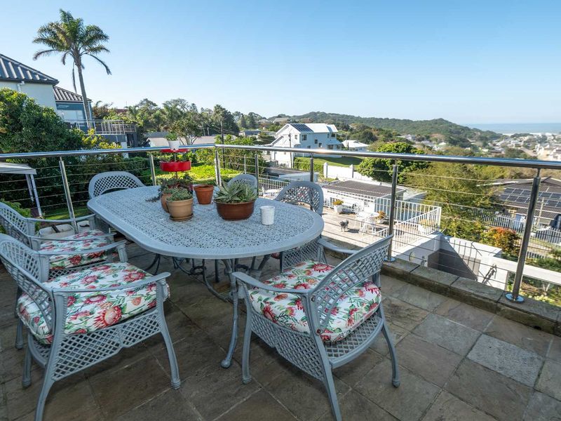 Spacious elevated balcony featuring stone tile flooring and a modern stainless steel balustrade, offering expansive coastal and neighbourhood views.