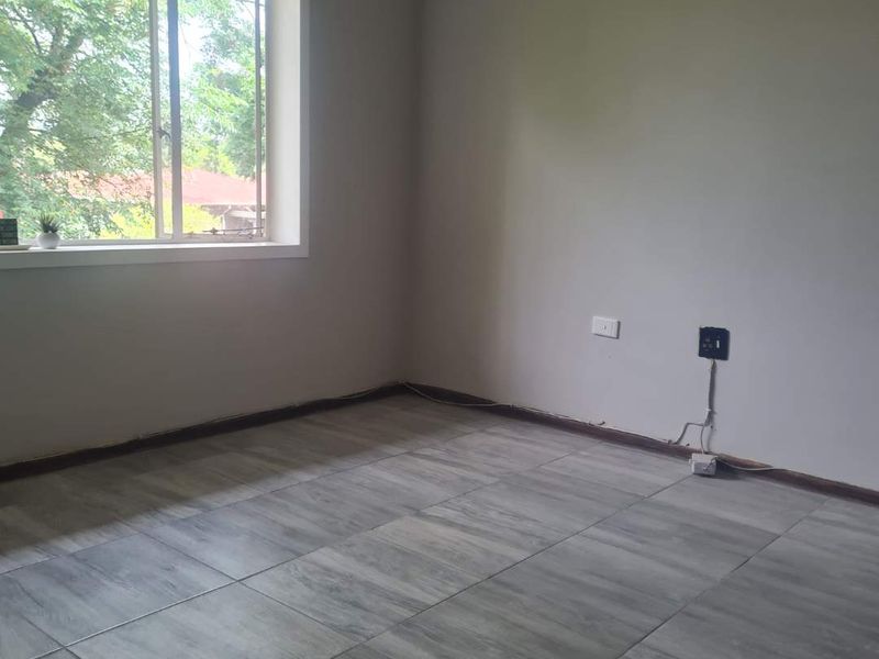 An empty bedroom featuring grey tiled flooring and a window with natural light, ready for personalization.